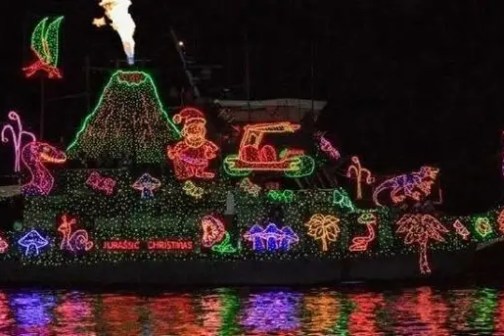Boat decorated with colorful Christmas lights, dinosaurs, volcano, palm trees, and Santa.