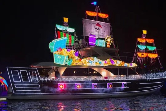 Festively decorated boat with colorful lights shaped like a pirate ship at night.