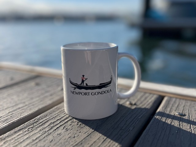 White mug with gondola design on wooden dock by water.