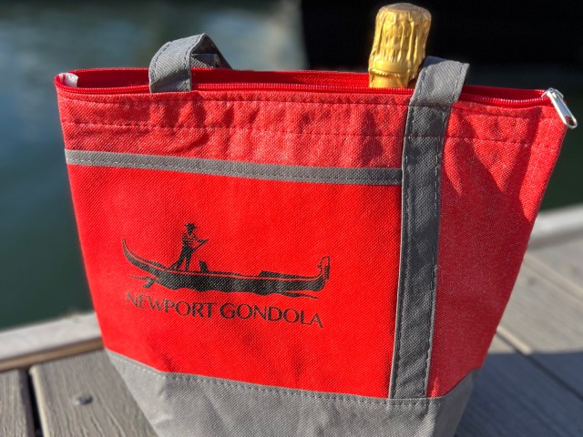 Red bag with 'Newport Gondola' and a champagne bottle by the water.