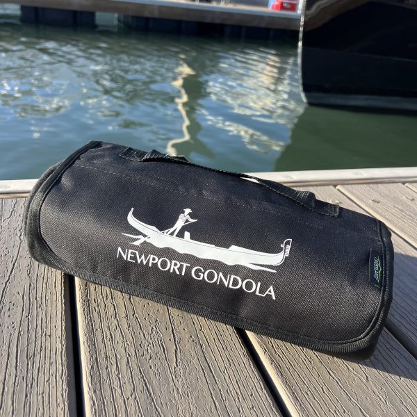 Black Newport Gondola bag on a wooden dock near water.