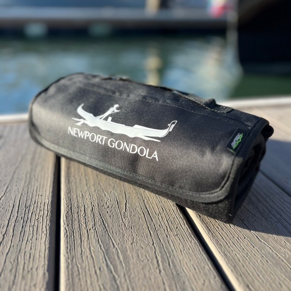 Black bag with 'Newport Gondola' logo on wooden dock near water.