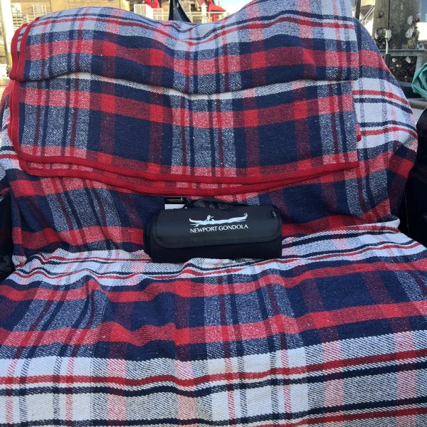 Plaid blanket on seat with Newport Gondola bag; rustic building in background.