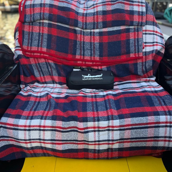 Plaid blanket on gondola seat with Newport Gondola case, water in background.